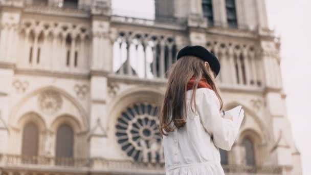 Un piccolo berretto d'artista che si avvicina alla Notre Dame di Parigi, Francia. Ragazza elegante facendo il suo hobby vicino alla famosa chiesa . — Video Stock