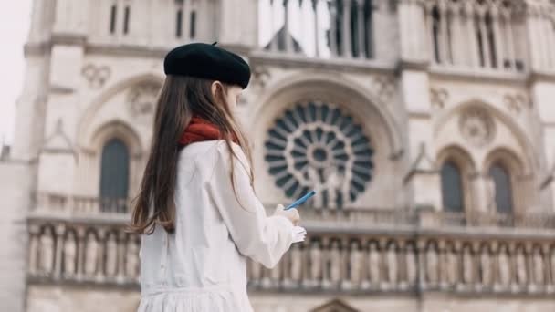 Seniman kecil dalam topi baret hitam dan syal merah menggambar di buku catatan dekat Notre Dame di Paris, Prancis, katedral terkenal . — Stok Video