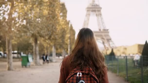 Back view of young woman walking with backpack near the Eiffel tower in Paris, France. Tourist enjoying the view.