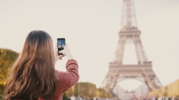 Vista trasera de una joven morena tomando fotos de la torre Eiffel en un smartphone. Adolescente explorando París, Francia . — Vídeos de Stock