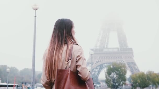 Vista trasera de la joven mujer con estilo caminando en el centro de París, Francia en la madrugada brumosa y se ve en la torre Eiffel . — Vídeo de stock