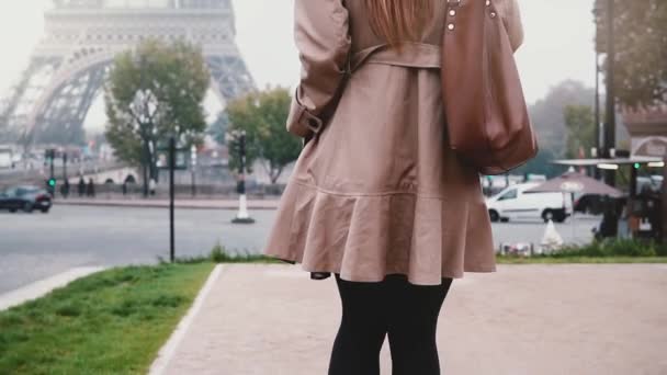 Νεαρή γυναίκα ευτυχισμένη περπατώντας στο κέντρο της πόλης στα ομιχλώδη ημέρα, κοντά στον Πύργο του Άιφελ στο Παρίσι, Γαλλία και χρησιμοποιώντας το smartphone. — Αρχείο Βίντεο