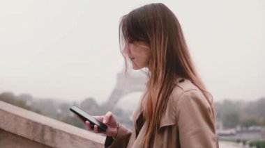 Smartphone, Paris'te Eyfel Kulesi'ne yakın duran kullanan genç kadın sosyal ağ sohbet. Fransa. Ağır çekim.
