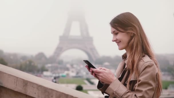 Młoda kobieta stylowe dzieje górę i za pomocą smartfona w pobliżu wieży Eiffla w Paryżu, Francja. Zwolnionym tempie. — Wideo stockowe