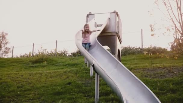 A menina feliz desce por uma tábua de correr. Movimento lento. Bonito criança feminina com cabelos longos no parque infantil verde de verão . — Vídeo de Stock
