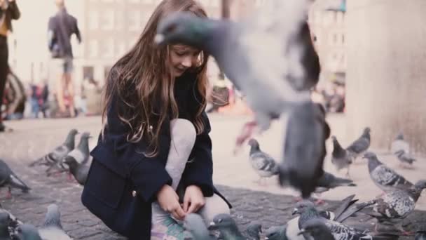 Beetje Kaukasische meisje zit voeding vogels buiten. Slow-motion. Gelukkig vrouwelijke kind voedt duiven in de straat. Vrede. — Stockvideo