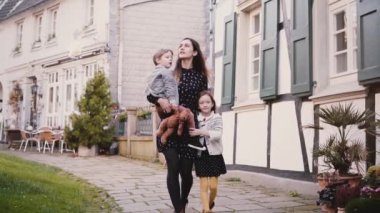 Güzel kadın iki çocuk ile birlikte yürür. Ağır çekim. Avrupa aile. Anne, erkek ve kız elele tutuşun. Beraberlik.