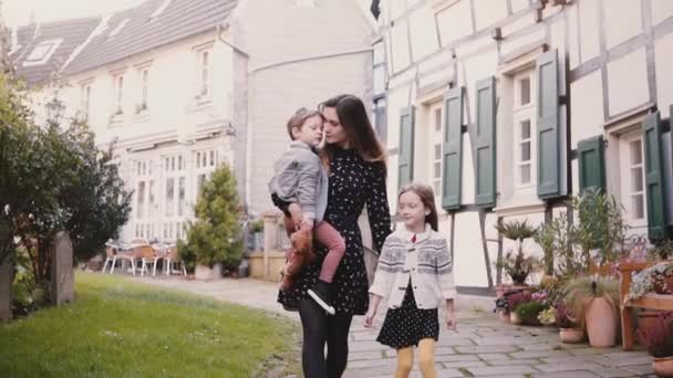 A família europeia anda em conjunto. Mãe e dois filhos. Movimento lento. Mulher, menino e menina dão as mãos sorrindo. Amor e cuidado . — Vídeo de Stock