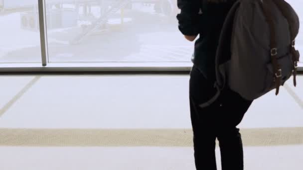 Chica con mochila camina a la ventana del aeropuerto salón. Pasajera con smartphone espera en terminal. Empresaria. 4K — Vídeo de stock