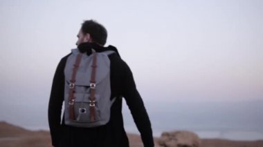 İnsan sırt çantası ile çölde yürüyor. Ağır çekim. Genç erkek alacakaranlıkta vahşi doğada tek başına dolaşır. Doğal dağ gökyüzü. İsrail