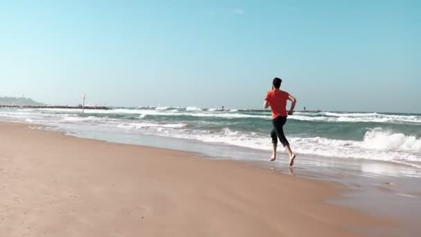 El joven corre a orillas del mar. Playa de verano. Concepto de libertad. Hombre europeo disfrutando de vacaciones. Mediterráneo 4K — Vídeo de stock