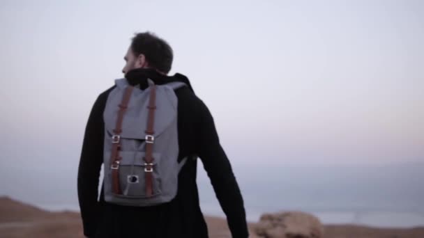 Um homem com mochila caminha no deserto. Movimento lento. Um jovem vagueia sozinho no deserto do crepúsculo. Céu de montanha cênico. Israel — Vídeo de Stock