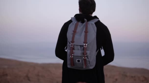 夕暮れの砂漠で一人佇むバックパックを持つ男。スローモーション。旅行者は、夕焼け空を見てします。インスピレーションを探してください。. — ストック動画
