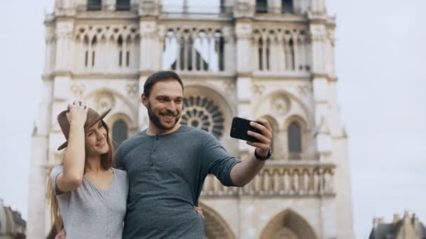 Jovencita feliz parada cerca de Notre Dame en París, Francia y tomando fotos de selfies en un smartphone . — Vídeos de Stock