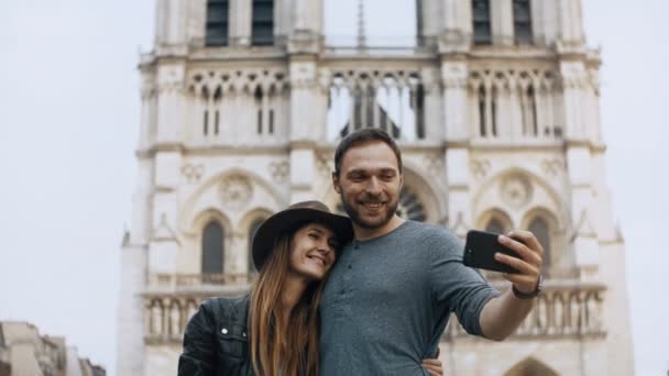 Счастливая молодая пара, стоящая возле Нотр-Дама в Париже. Франция и фотографирование селфи на смартфон . — стоковое видео