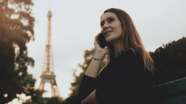 Yalnız Paris, Fransa'da Eyfel Kulesinin yakınında bankta oturmuş ve smartphone kullanarak genç mutlu kadın.