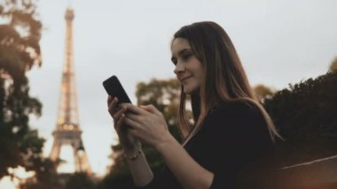 Belgili tanımlık smartphone kullanarak güzel ve genç birbayan. Mutlu erkek Paris, Fransa'da Eyfel Kulesinin yakınında bankta oturmuş.