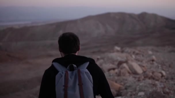 Ο άνθρωπος με το σακίδιο περπατά μόνος στο σούρουπο έρημο. Αργή κίνηση. Καταπληκτικό ηλιοβασίλεμα στα βουνά τοπίο. Ψάχνοντας για έμπνευση. — Αρχείο Βίντεο