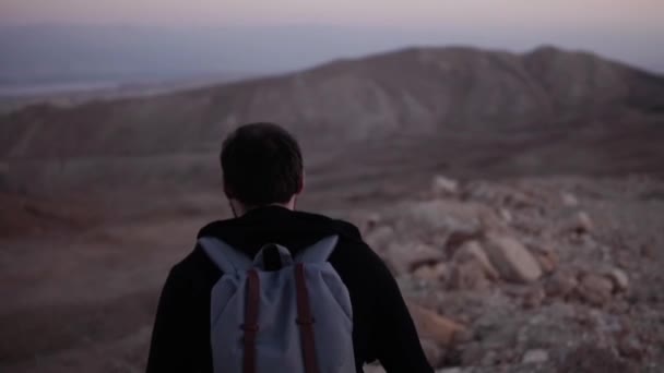 Sırt çantası ile insan yalnız alacakaranlıkta çölde yürüyor. Ağır çekim. Şaşırtıcı günbatımı dağlar sahne. İlham için arama. — Stok video