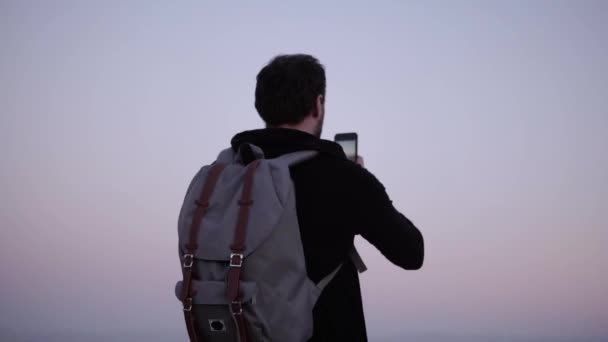 Kaukasische man geniet van verbazingwekkende bergpanorama. Slow-motion. Opgewonden toeristische neemt smartphone foto's van violet schemering hemel. — Stockvideo