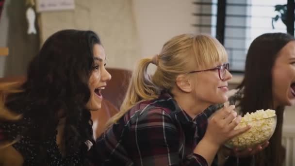 Meninas caucasianas felizes assistir programa de TV. Movimento lento. Emoção. Lindas senhoras assistindo jogo de esportes com pipocas em casa . — Vídeo de Stock