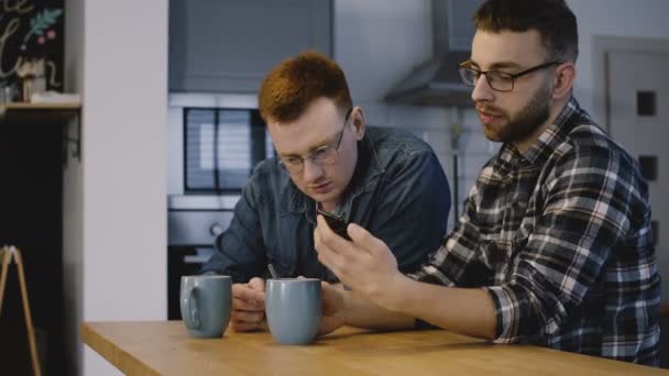 Due ragazzi europei parlano usando lo smartphone insieme. Partner startup discutono nuove idee in cucina ufficio. 4K . — Video Stock