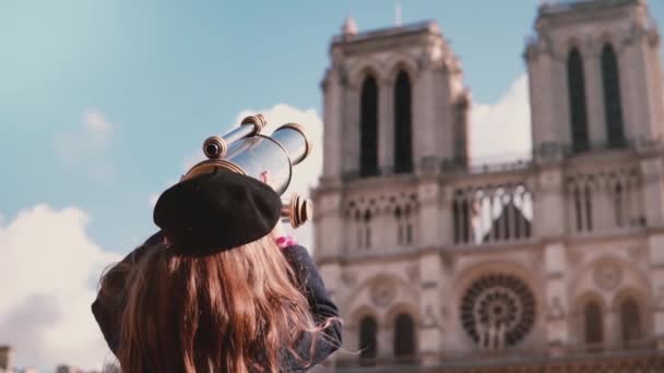 Ragazza in berretto guarda attraverso binocolo moneta. Al rallentatore. Notre-Dame de Paris. Femmina bambino utilizzando telescopio vista . — Video Stock