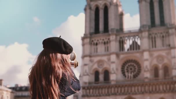 Menina de boina usando telescópio operado por moedas. Movimento lento. Notre Dame de Paris. Binóculos estacionários. Férias . — Vídeo de Stock