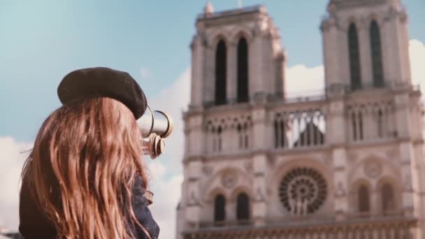 A criança de menina na boina olha por binóculos de moeda. Movimento lento. Notre-Dame de Paris. Telescópio operado por moedas. Turismo . — Vídeo de Stock