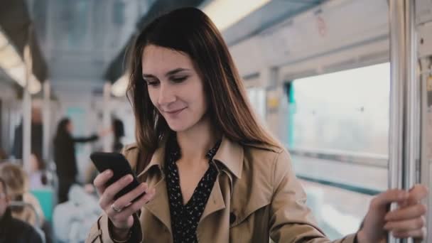 Καυκάσιος γυναίκα χρησιμοποιώντας το smartphone στο αυτοκίνητο του υπόγειου σιδηρόδρομου. Όμορφη happy νεαρό Γραφείο εργαζόμενος ανάγνωση ειδήσεων από κινητό app. 5g. 4k — Αρχείο Βίντεο
