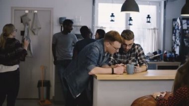 İki adam akıllı telefon app office mutfağa kullanın. Farklı bir partide sosyal ağları kullanarak mutlu genç Avrupa büyükler. 4k.