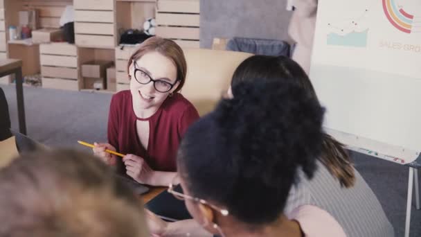 女性チーム リーダーは、職場の同僚をガイドします。多民族のオフィスでチームワークのミーティングで話す女性実業家。4 k — ストック動画