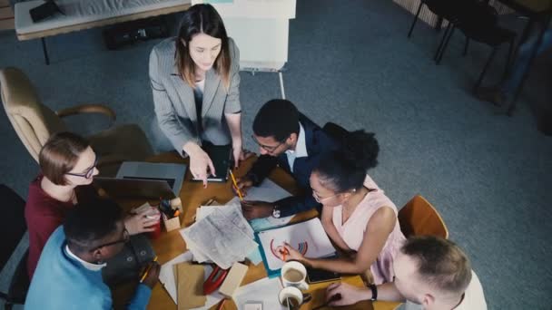 Vue de dessus mixte collègues de course travaillant à la table dans le bureau moderne à la mode. Patron féminin dirigeant une équipe diversifiée réunion 4K 