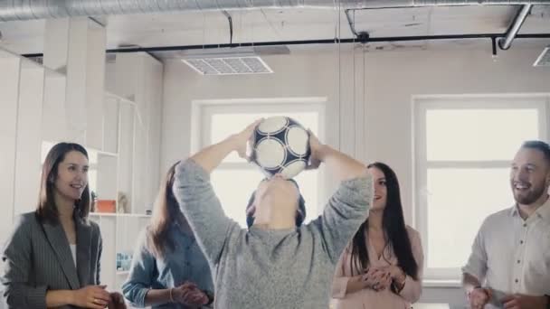 Счастливый азиат пытается жонглировать футболом. Позитивные смешанные этнические работники играют в забавные спортивные игры в офисе 4K — стоковое видео