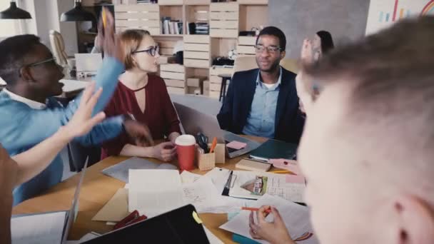 El grupo multiétnico celebra el éxito en la reunión. Jóvenes empleados felices aplauden, dan chocos y levantan los brazos 4K . — Vídeos de Stock