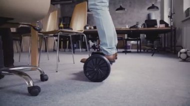 Kamera hoverboard modern ofisindeki erkek bacakları takip. Genç işadamı Segway kapalı, meet takım 4 k taşımak için kullanarak.
