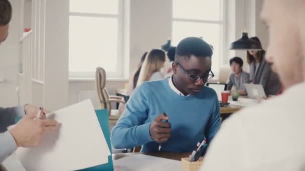 Konsantre Afrikalı-Amerikalı genç adam mimari kroki üzerinde popüler ofis alanı 4 k meslektaşları ile çalışkan. — Stok video