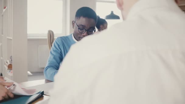 Deux jeunes hommes heureux métis coopèrent sur un projet d'entreprise dans un bureau élégant à la mode, rient, puis se concentrent à nouveau 4K .