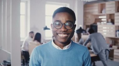 Kameraya gülümseyen gözlük yakışıklı genç Afro-Amerikalı işadamı. 4 k poz hipster şık erkek ofis çalışanı.