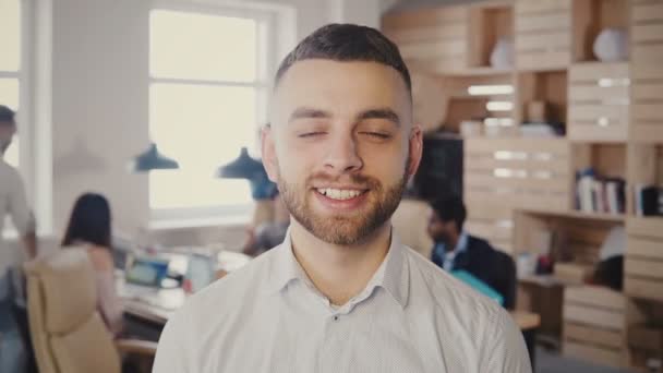 Retrato de un joven feliz hombre de negocios caucásico posando en una oficina ocupada. Hermoso trabajador creativo masculino mirando la cámara 4K . — Vídeo de stock