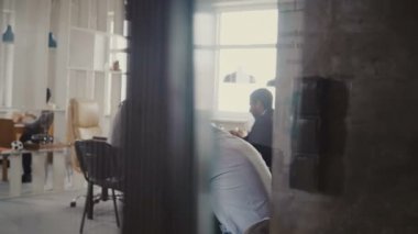 Genç adam akıllı telefon kullanma modern office Dolly vurdu. Cam duvarı, 4 k arka planda toplantı çok ırklı görüntülemek