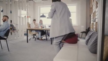 Dolly shot iki kadın meslektaşlarının ofis kanepe kalkmak, modern ofiste walk away. 4 k cam duvardan görüntülemek.