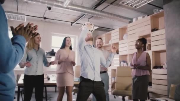 Happy Caucasian manager faz malabarismos com futebol na cabeça. Funcionários multiétnicos alegres celebram o sucesso no escritório em câmera lenta — Vídeo de Stock