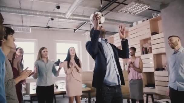 Gelukkig zwarte teamleider jongleert voetbal op hoofd. Multi-etnisch opstarten werknemers vieren succes in office slow motion — Stockvideo