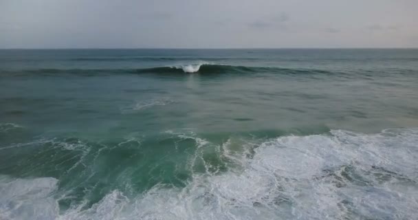 Drone volant juste au-dessus de grandes vagues océaniques bleues sauvages se précipitant vers le rivage, moussant et s'écrasant sous un ciel nuageux sombre .