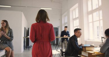 Kamera kendinden emin orta yaşlı kadın patronu takip ediyor. Çok ırklı iş adamlarını aydınlık ve rahat bir çatı katında motive ediyor.