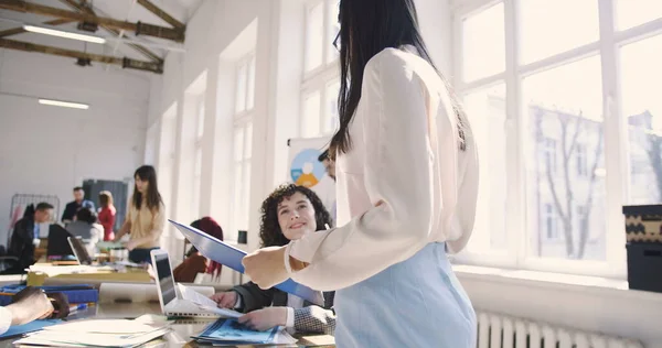 Elegante joven confiada líder de equipo mujer en gafas dando instrucciones a colegas multiétnicos en la oficina moderna . — Foto de Stock