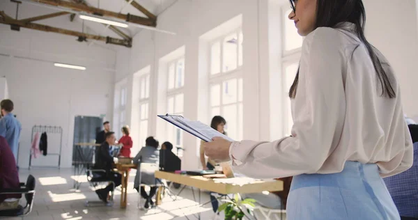 Elegante joven confiada líder de equipo mujer en gafas dando instrucciones a colegas multiétnicos en la oficina moderna . — Foto de Stock