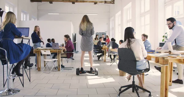 Cámara sigue confiado líder femenino utilizando scooter eléctrico para moverse por la oficina loft moderno. Lugar de trabajo saludable . — Foto de Stock