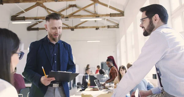 Felice uomo d'affari europeo di mezza età che parla con giovani dipendenti multietnici, controllando il processo di lavoro presso l'ufficio alla moda — Foto Stock